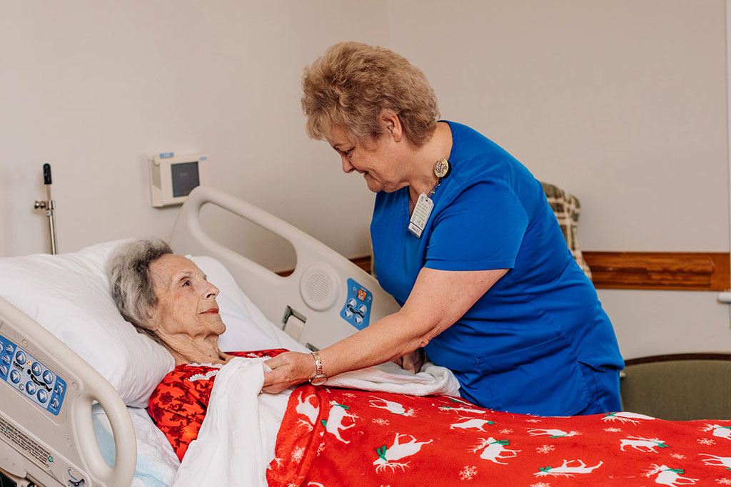 A Caregiver Tucking An Elderly Woman Into Bed