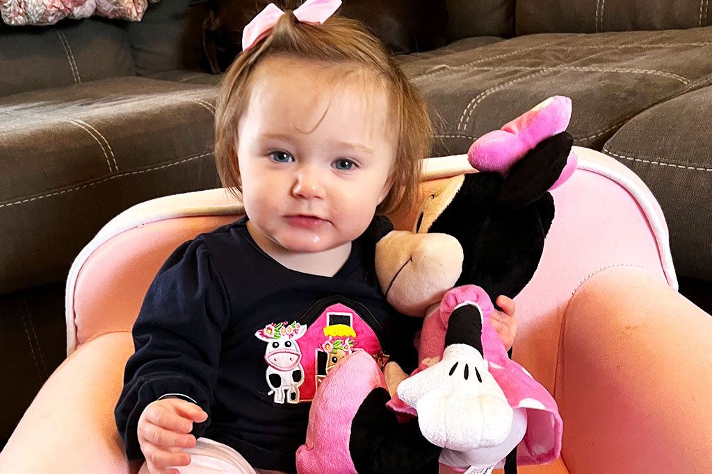 A Young Girl Sitting In A Pink Chair Holding A Plush Doll