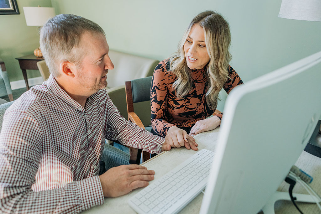 A Woman Holding A Man's Hand Who Is Sitting At A Computer