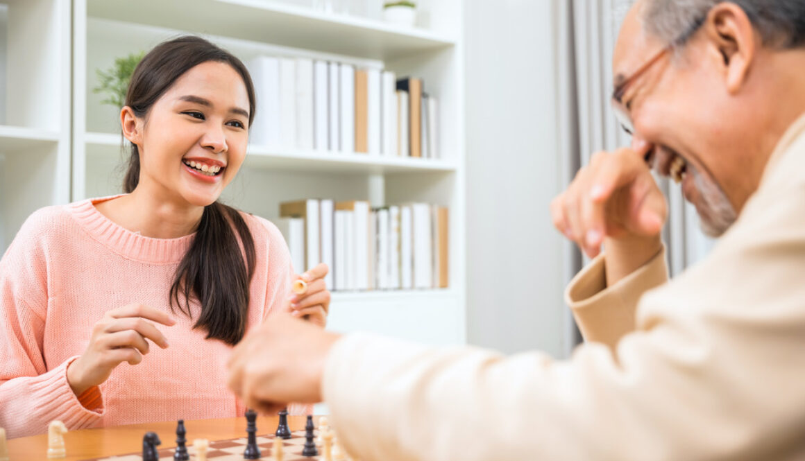 Asian Woman Playing Chess With Elderly Man As Part of Summer Volunteer Programs