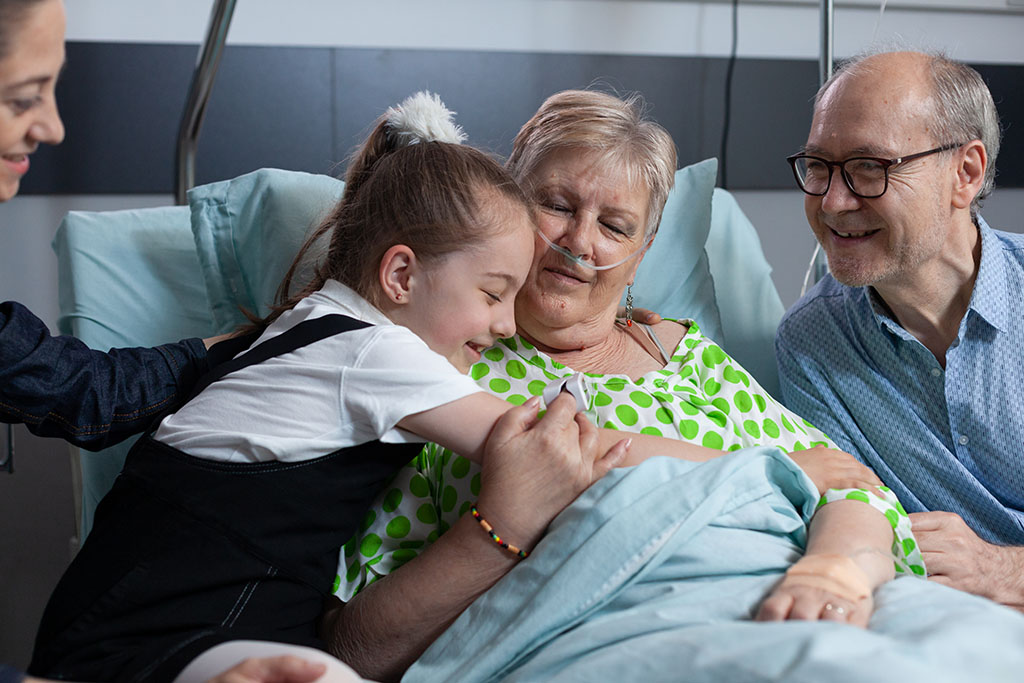 A Child Hugging An Elderly Woman Who Is Laying In A Hospital Bed Should You Take A Child To Visit A Relative In Hospice