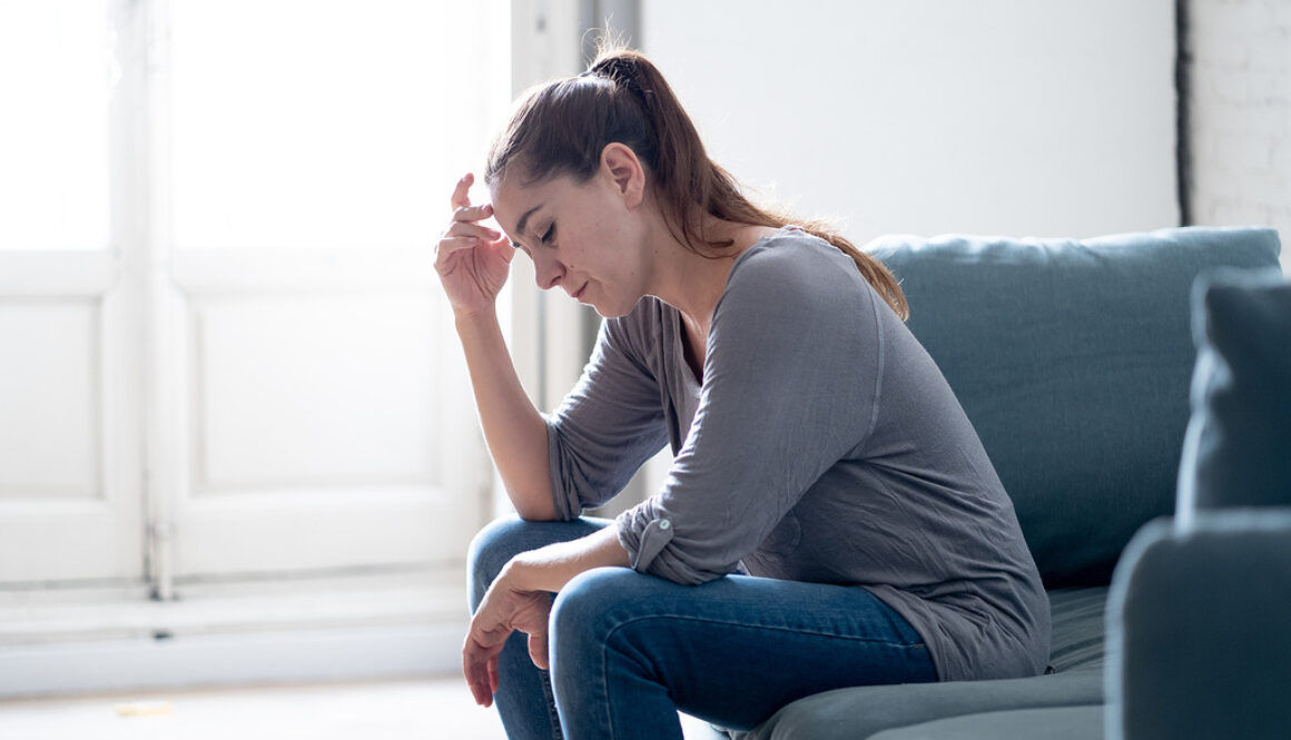 A Young Woman Sitting on a Couch Stressed Holding Her Head Dealing with Caregiver Burnout