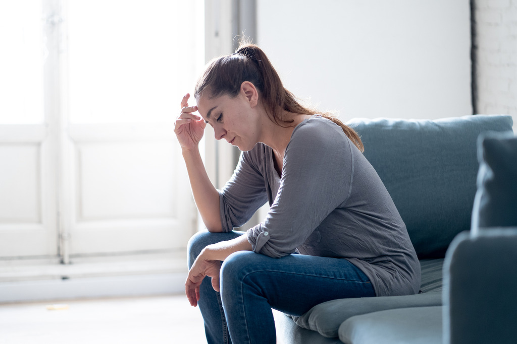 A Young Woman Sitting on a Couch Stressed Holding Her Head Dealing with Caregiver Burnout