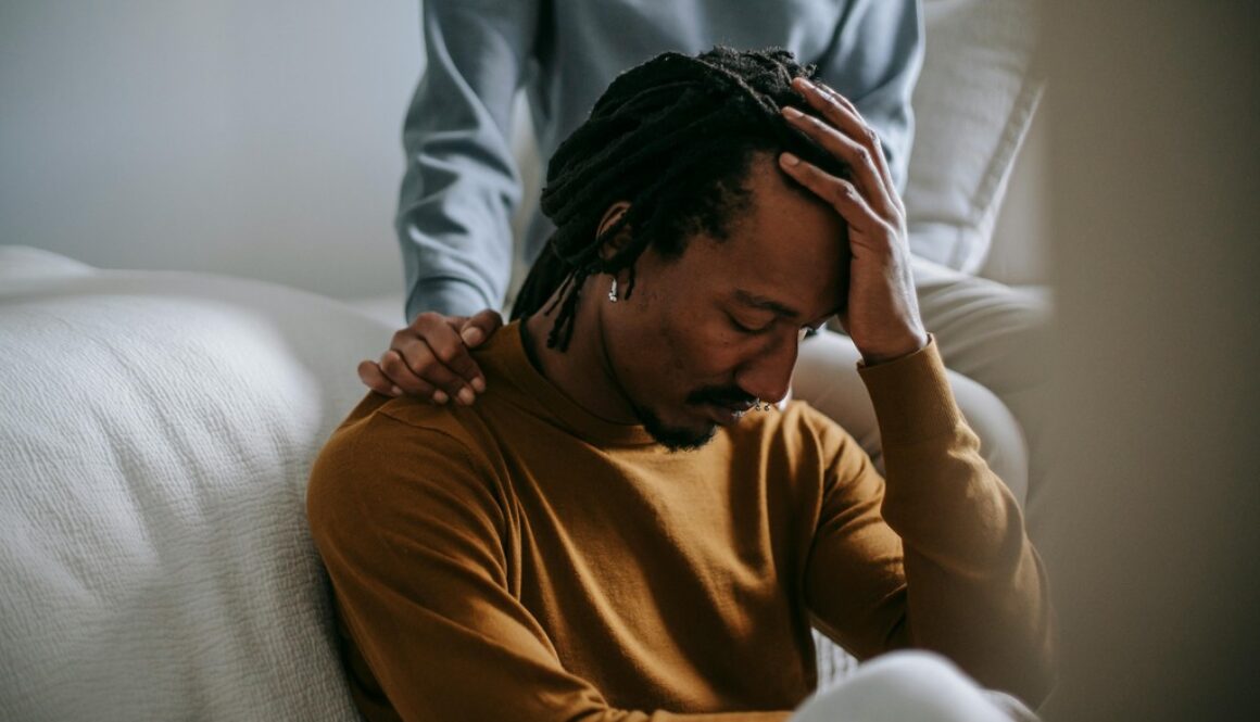 An African American Man Sad Holding His Head While Being Comforted by a Woman Self Care During Grief