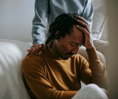 An African American Man Sad Holding His Head While Being Comforted by a Woman Self Care During Grief