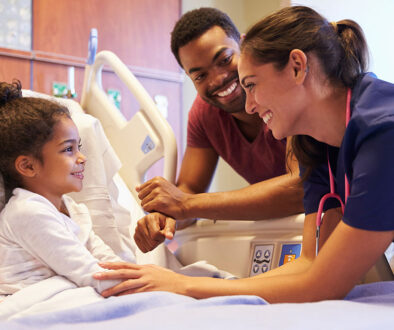 A Young African American Child Smiling at Her Dad & a Pediatrician Standing Beside Her While Laying in a Hospital Bed Pediatric Pain Management